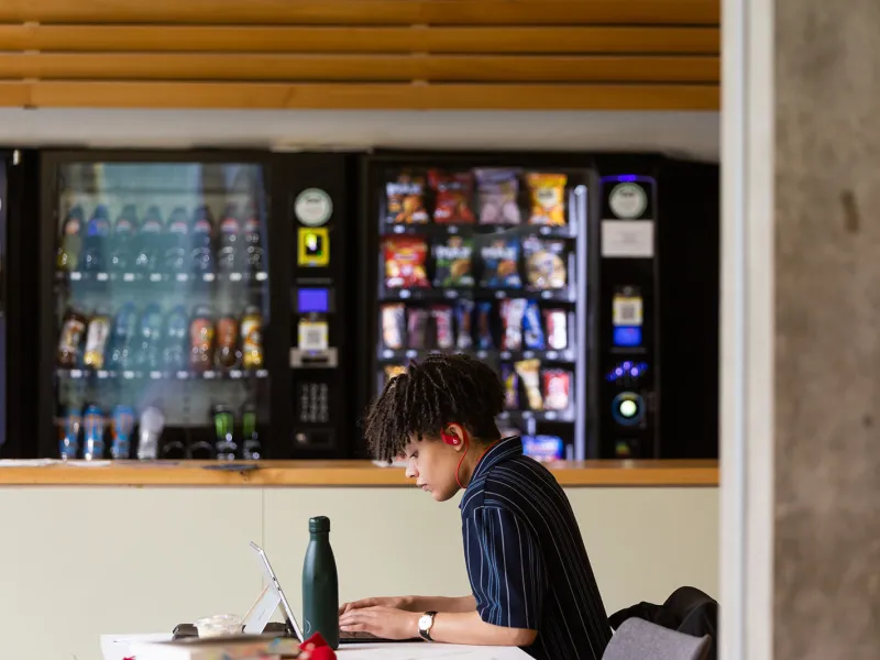 student working at laptop in front of vending machines