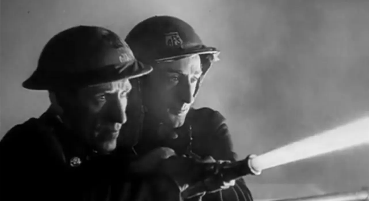 two 1940s firefighters hold a hose shooting out water