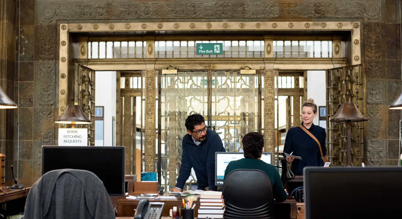 two readers speaking to a librarian at the readers desk in the University Library