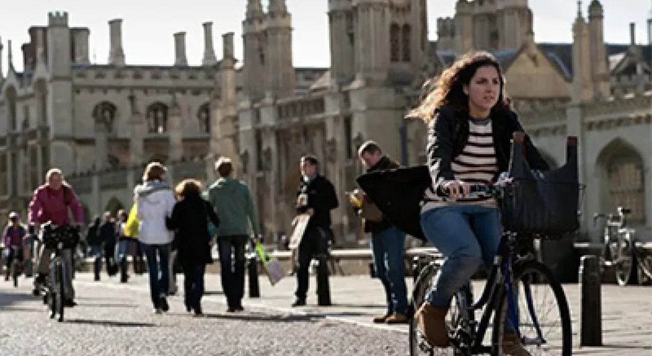 student cycling past King's college on cobbled street