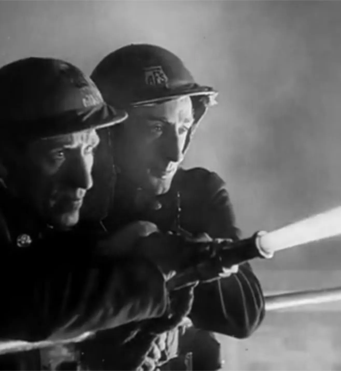 two 1940s firefighters hold a hose shooting out water