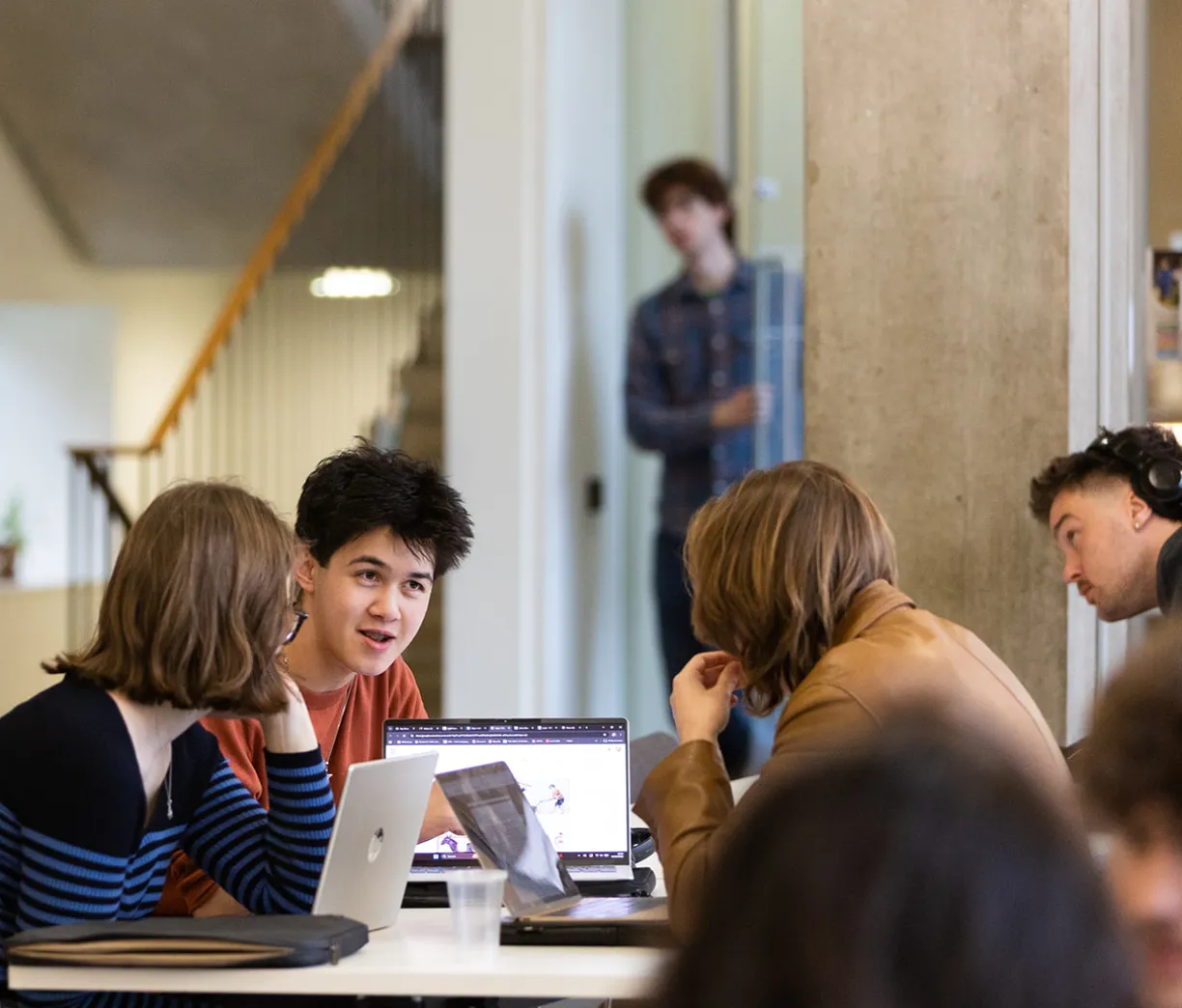 three students talking around a table, laptops in front of them