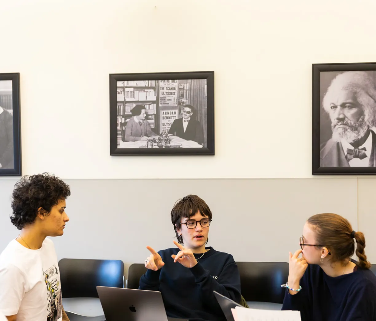 three students in discussion beneath three pictures