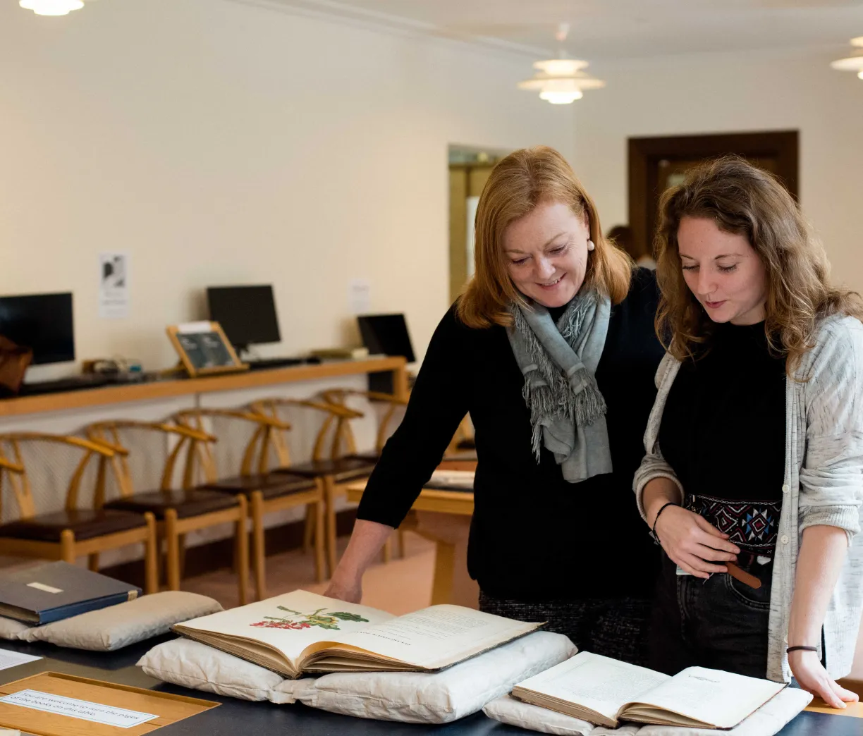Two people look at a large printed book with botanical book plates