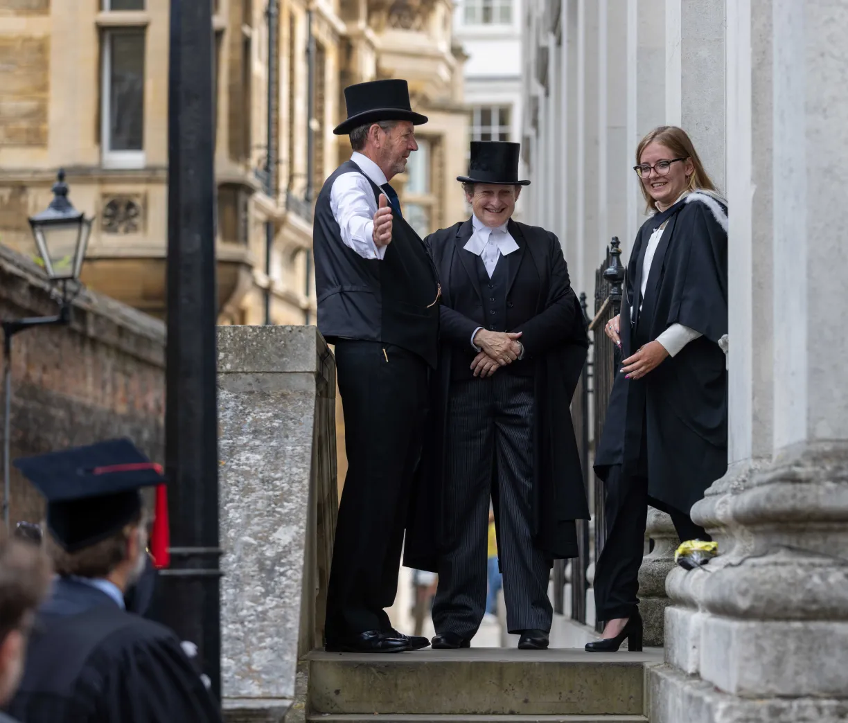 Two staff members are directing a graduate walking out of the Senate House during their graduation celebrations. Copyright: University of Cambridge (June 2024)