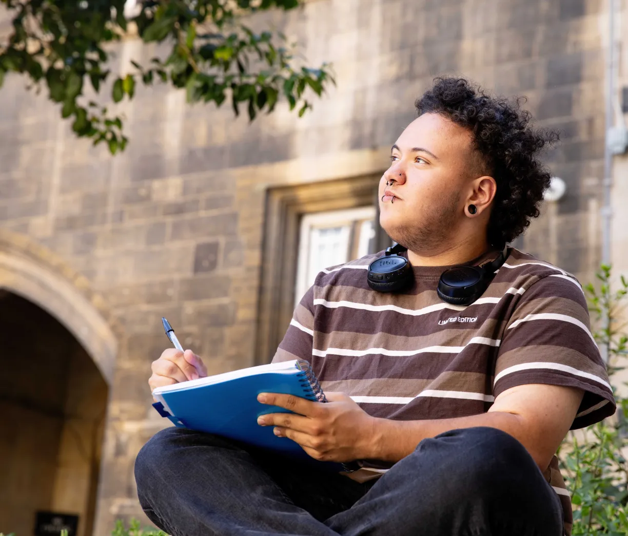 A University of Cambridge student sitting outside the Student Services Centre (SSC) with a notebook and studying. Copyright: University of Cambridge (June 2025).