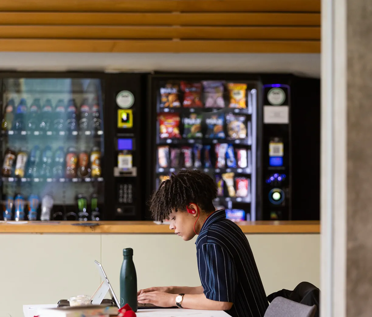 student working at laptop in front of vending machines